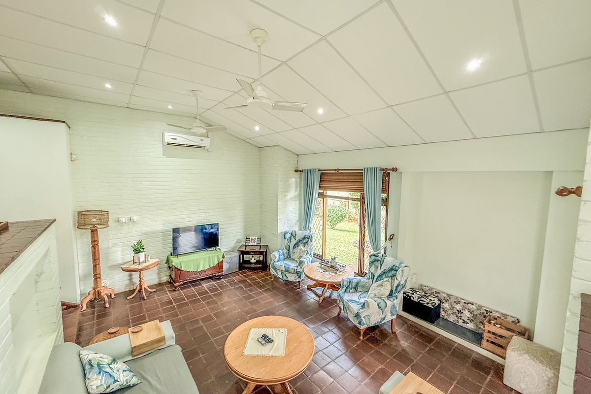 Spacious living room featuring vaulted ceilings, tiled flooring, split-system air conditioning, and direct access to the garden through large windows.