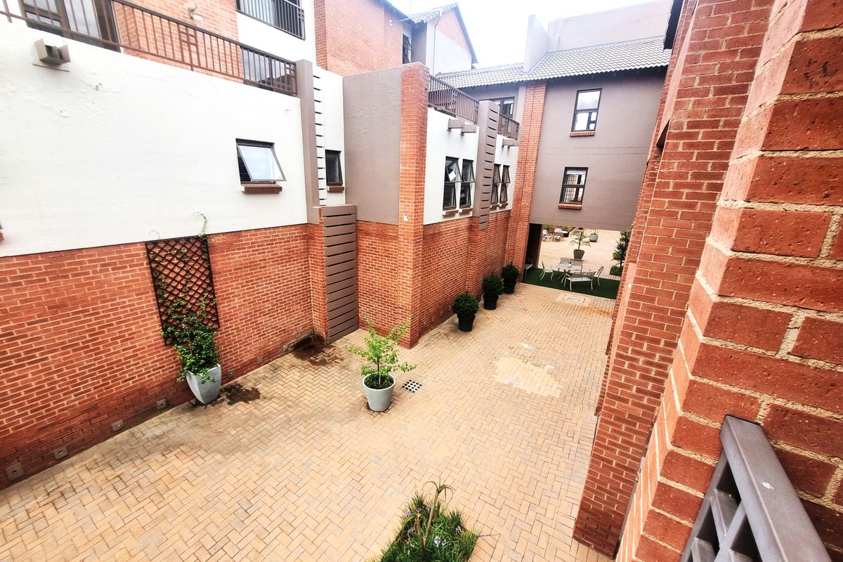 A view of the rear courtyard area featuring brick paving, face brick walls, and access to upper-level balconies within the apartment complex.