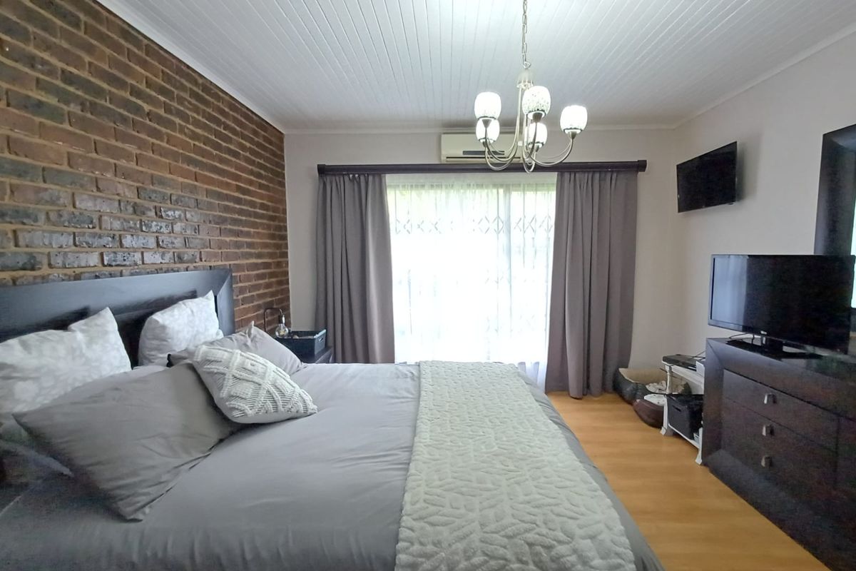 Spacious bedroom featuring an exposed brick feature wall, timber laminate flooring, and a split system air conditioner for climate control.