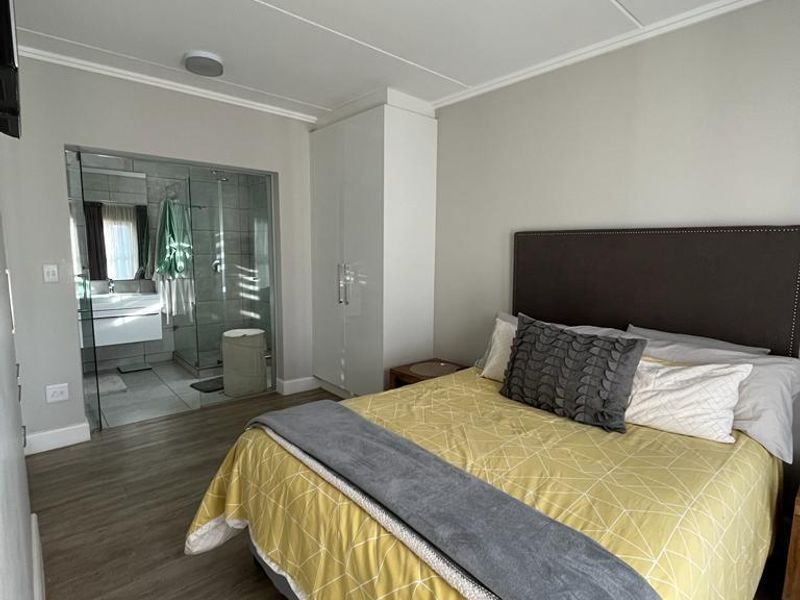 A well-maintained bedroom featuring wood-look flooring, built-in cabinetry, and an en-suite bathroom with a glass-enclosed shower.