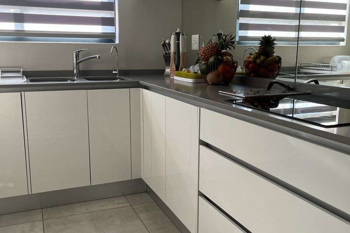 Modern kitchen featuring sleek white cabinetry, stone countertops, a mirrored backsplash, integrated hob, and large format floor tiles.