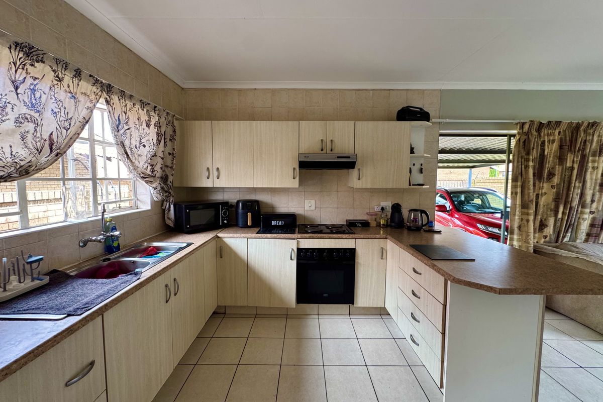 Functional kitchen featuring light wood-finish cabinetry, laminate countertops, built-in oven with extractor fan, and tiled flooring, offering a practical layout for daily use.