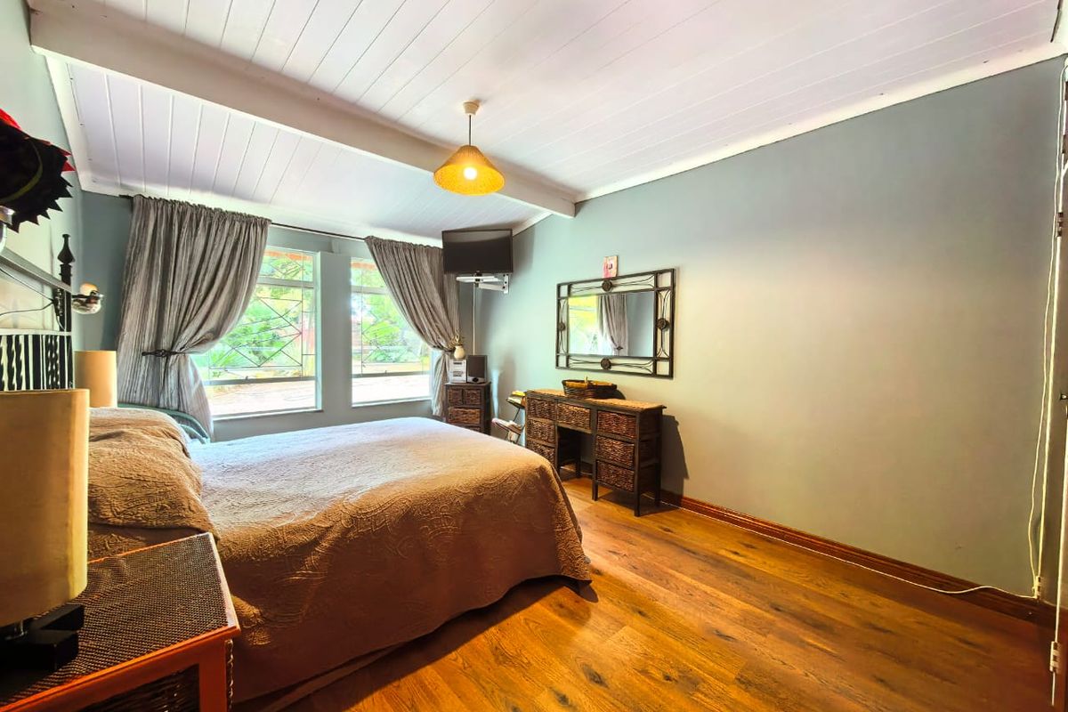 A bedroom featuring timber-look flooring, a white painted timber-paneled ceiling, and large windows with security bars.