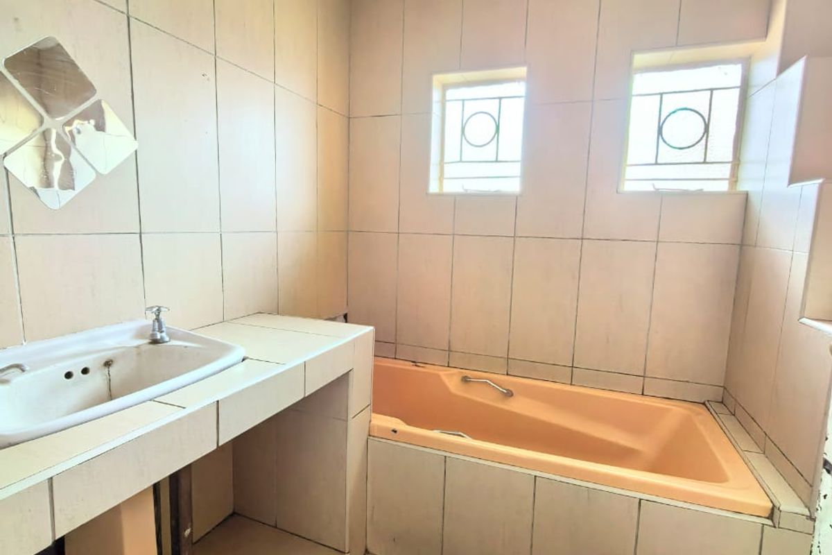 A dated bathroom featuring a built-in vanity with a basin and a peach-colored bathtub with tiled surround.