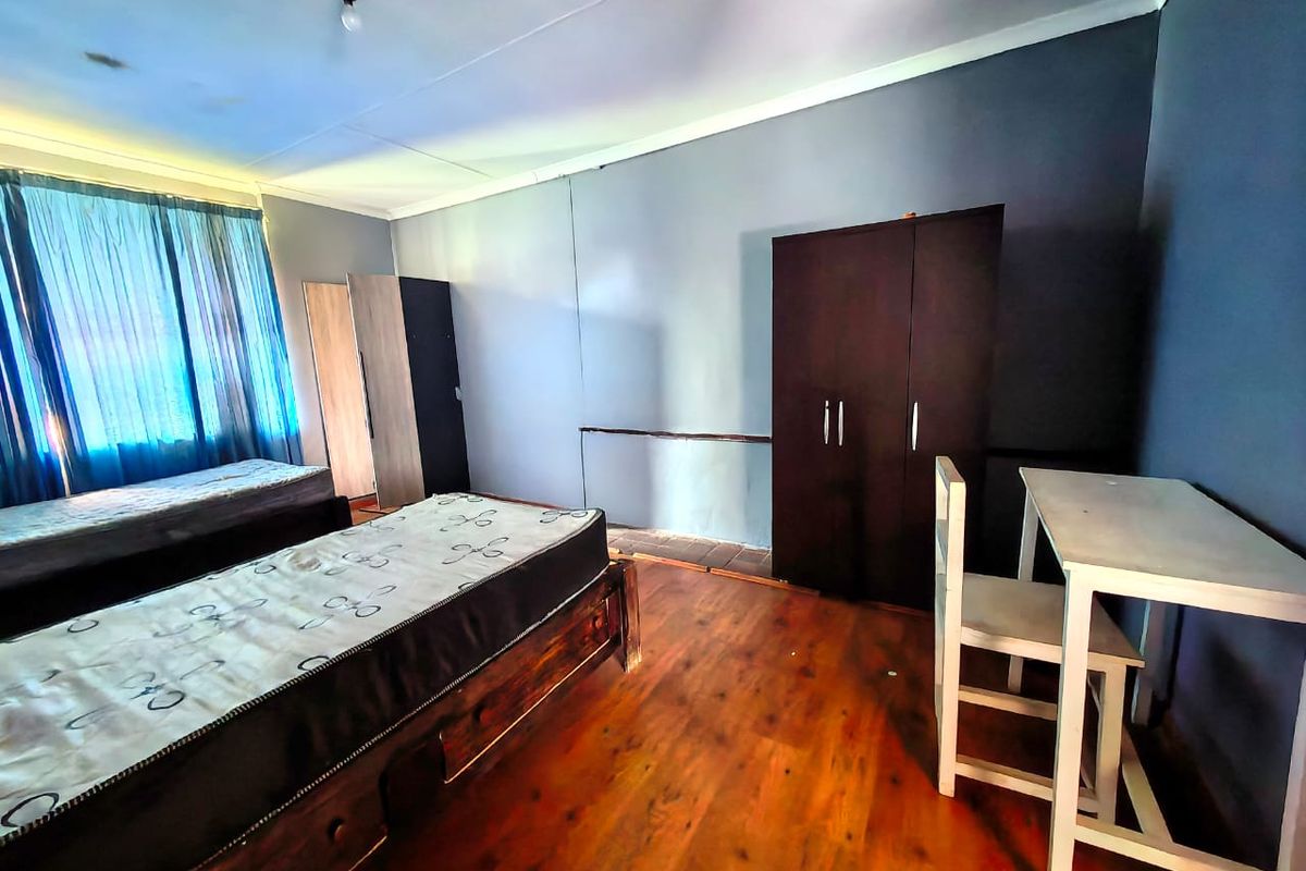 A bedroom featuring wood-look flooring, blue-toned walls, and a large window with curtains, providing a functional living space.