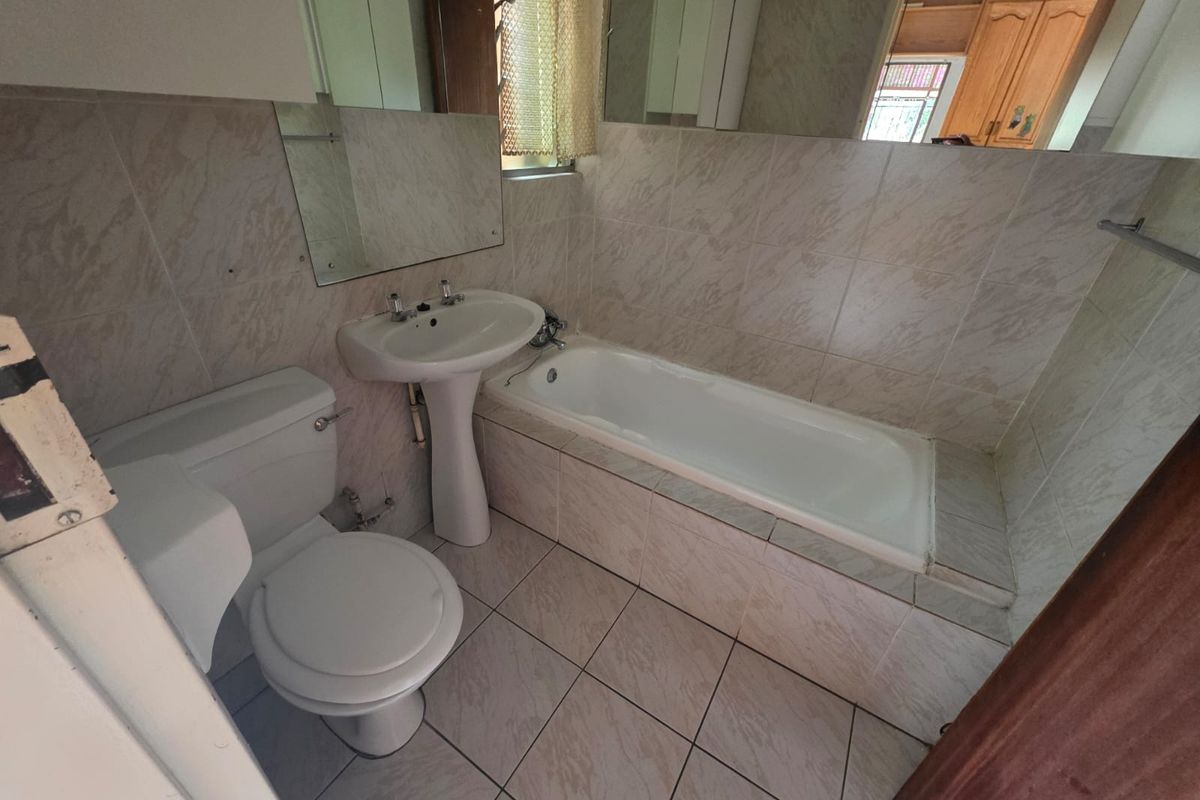 A functional bathroom featuring a built-in bathtub, pedestal basin, and toilet with neutral wall and floor tiling.