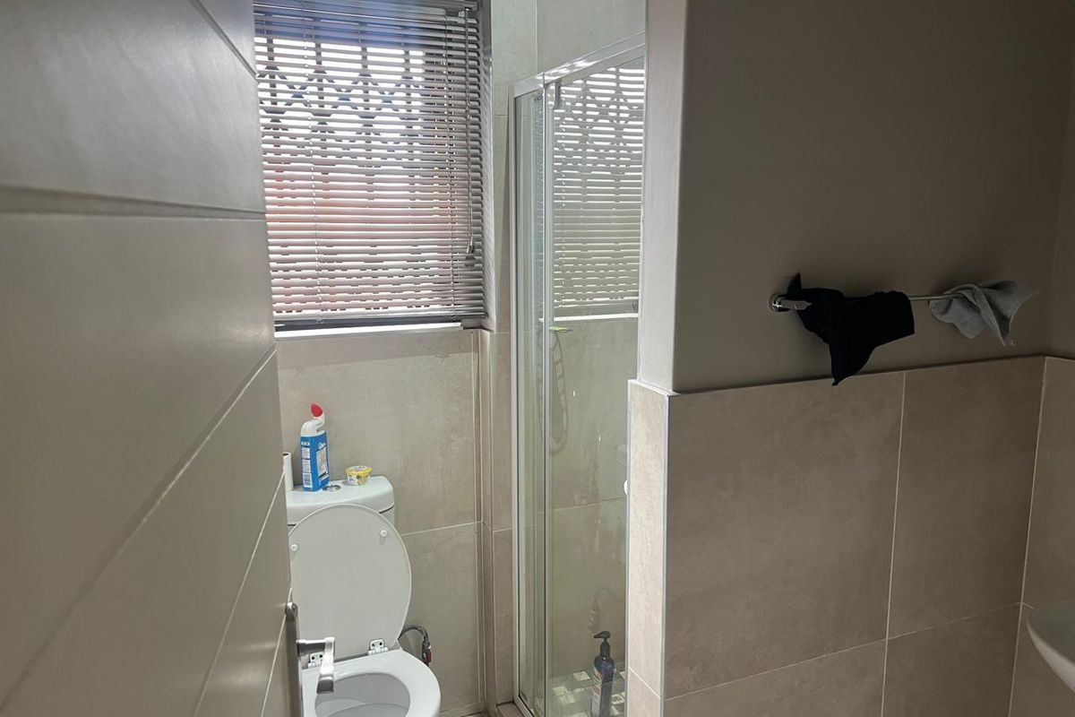 A modern bathroom featuring tiled walls, a glass-enclosed shower, and a toilet with fitted venetian blinds.