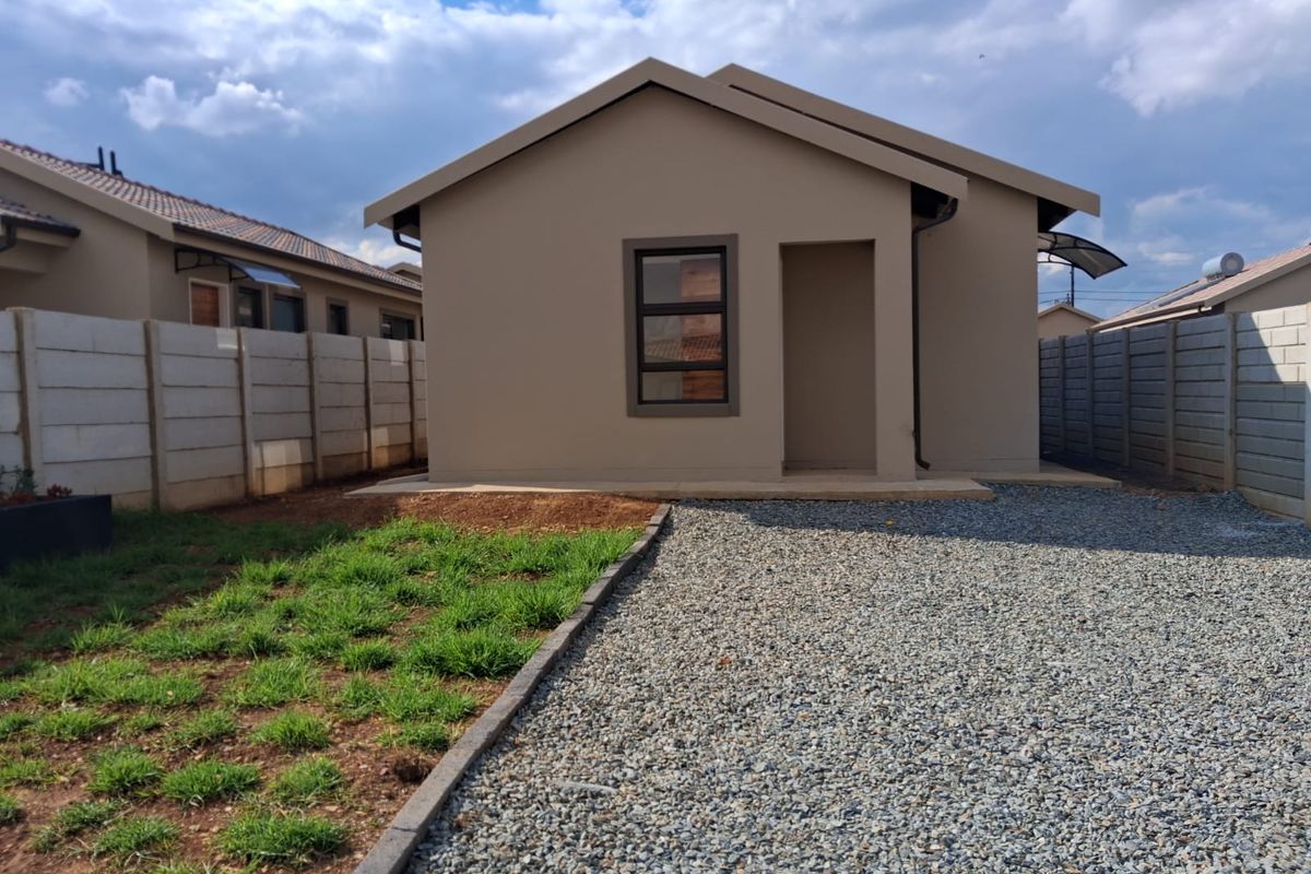 Rear view of a modern detached house featuring a gravel driveway, concrete boundary walls, and a small patch of lawn.