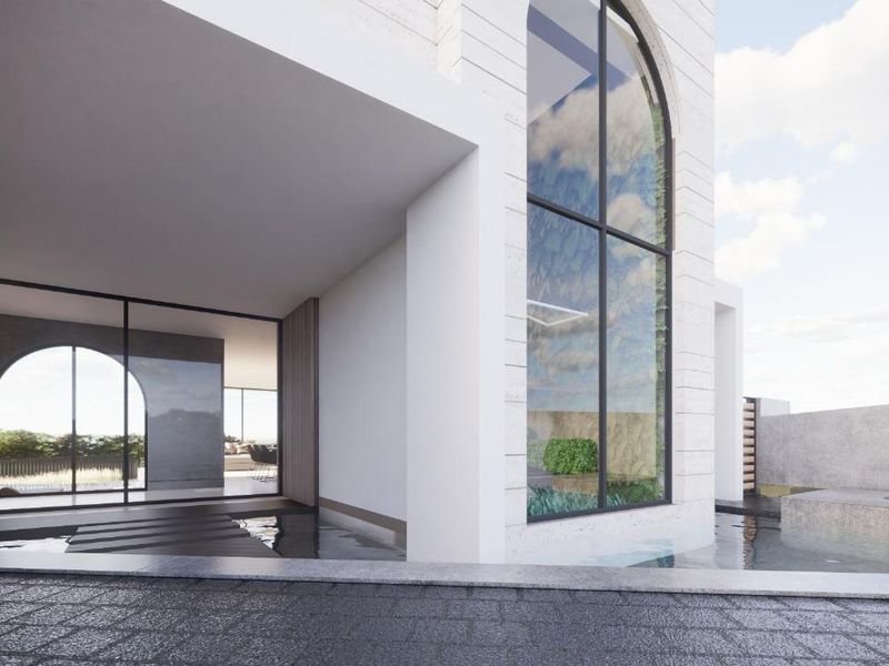 Modern architectural rear elevation featuring a covered patio, large arched window, and integrated water feature with stone finishes.