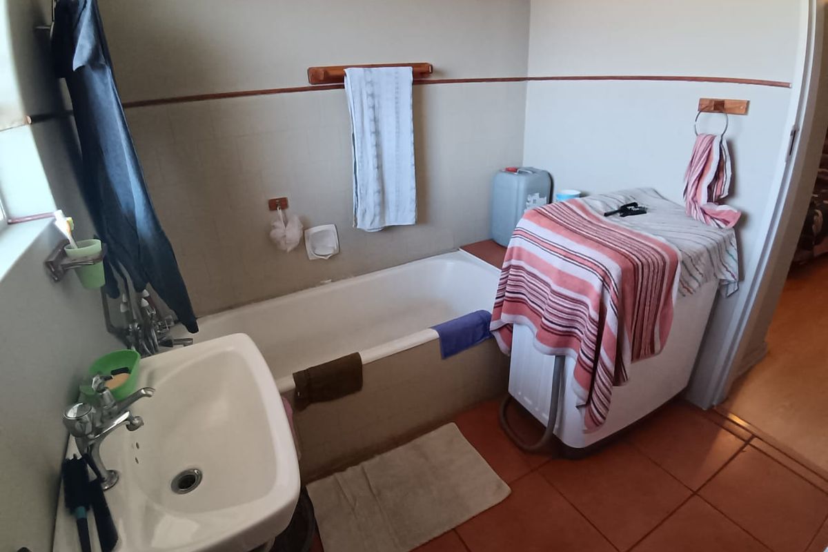A functional bathroom featuring a standard bathtub, pedestal basin, and space for a washing machine, finished with terracotta-style floor tiles.