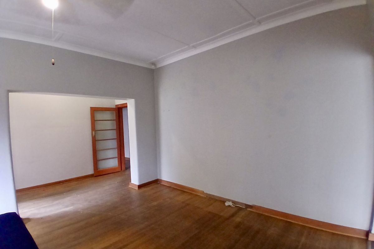 Spacious living area featuring original timber flooring, high ceilings with decorative cornicing, and a classic timber-framed glass door leading to an adjoining room.