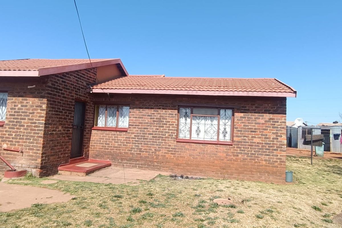 A single-story face-brick house featuring a tiled roof, security bars on windows, and a spacious rear yard area.
