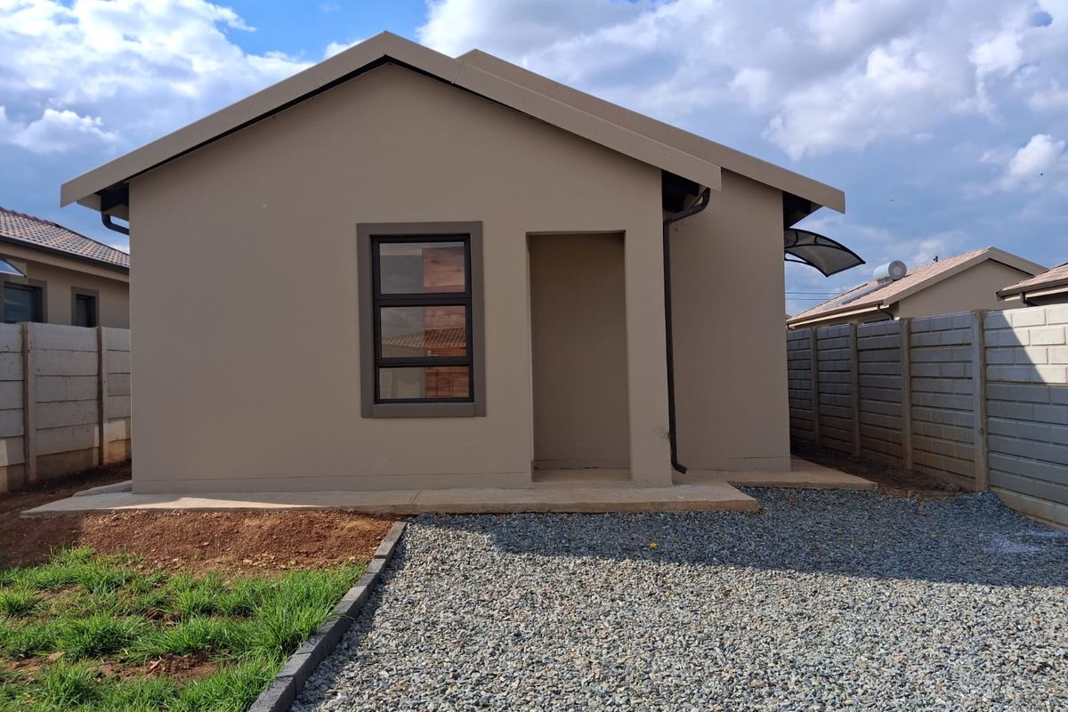 A view of the rear exterior of the house, featuring a concrete patio area, gravel ground cover, and perimeter boundary walls.