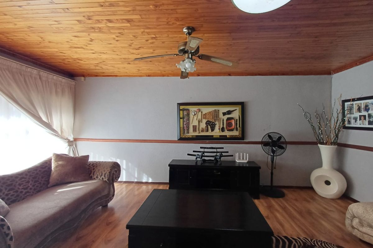 A living room featuring a timber-clad ceiling, laminate flooring, and a central ceiling fan, providing a functional and traditional living space.