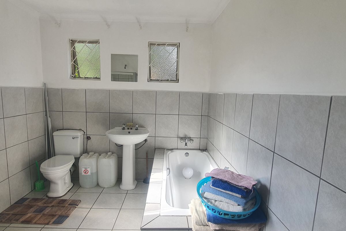 A functional bathroom featuring a pedestal basin, standard toilet, and a built-in bathtub with tiled walls and flooring.
