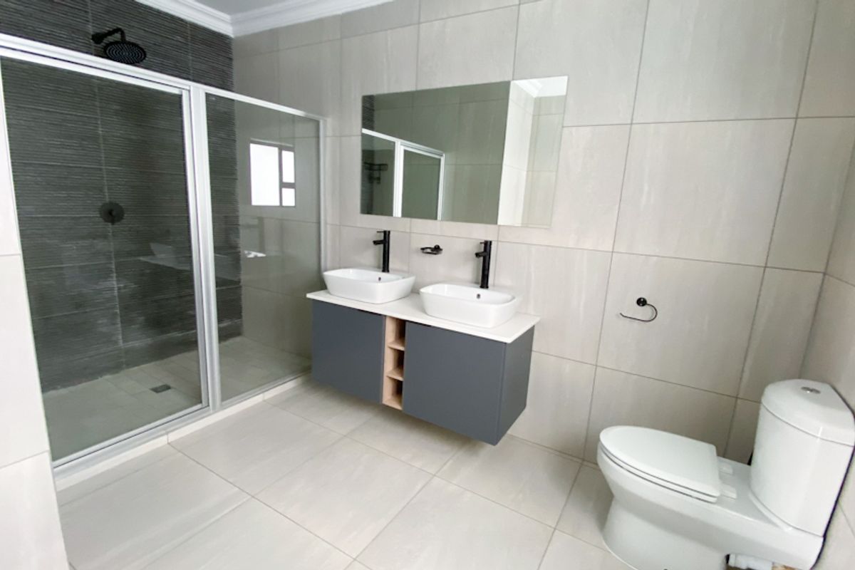 Modern bathroom featuring a double vanity with vessel sinks, a walk-in shower with glass enclosure, and contemporary wall-mounted toilet.