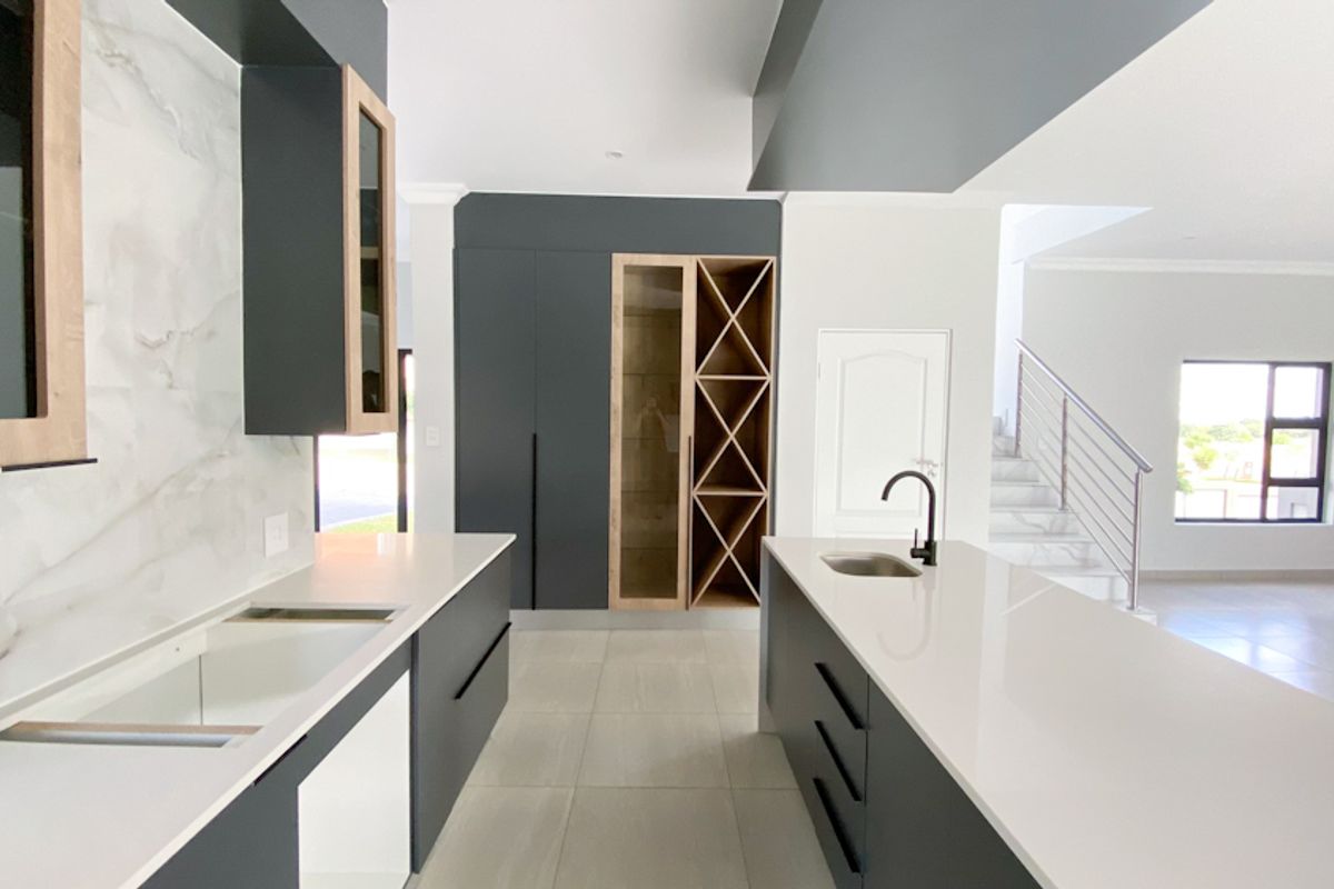 Modern kitchen featuring sleek dark cabinetry, light stone countertops, integrated wine rack, and a central island with a sink, overlooking an open-plan living area.