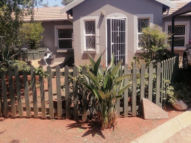 Front view of a townhouse featuring a gabled roof, security gate, and a small enclosed front garden area with paved driveway access.