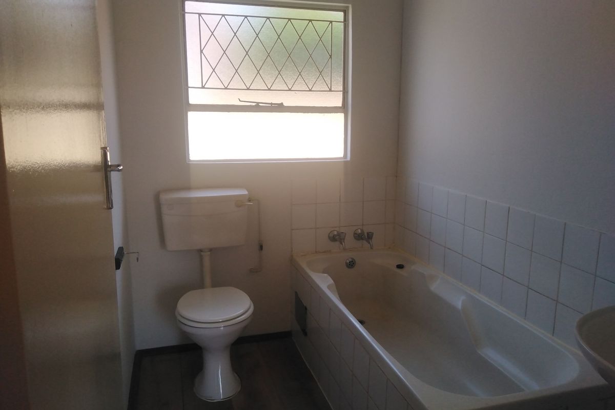A functional bathroom featuring a standard bathtub, toilet, and a window with security bars, offering a basic layout ready for modernization.