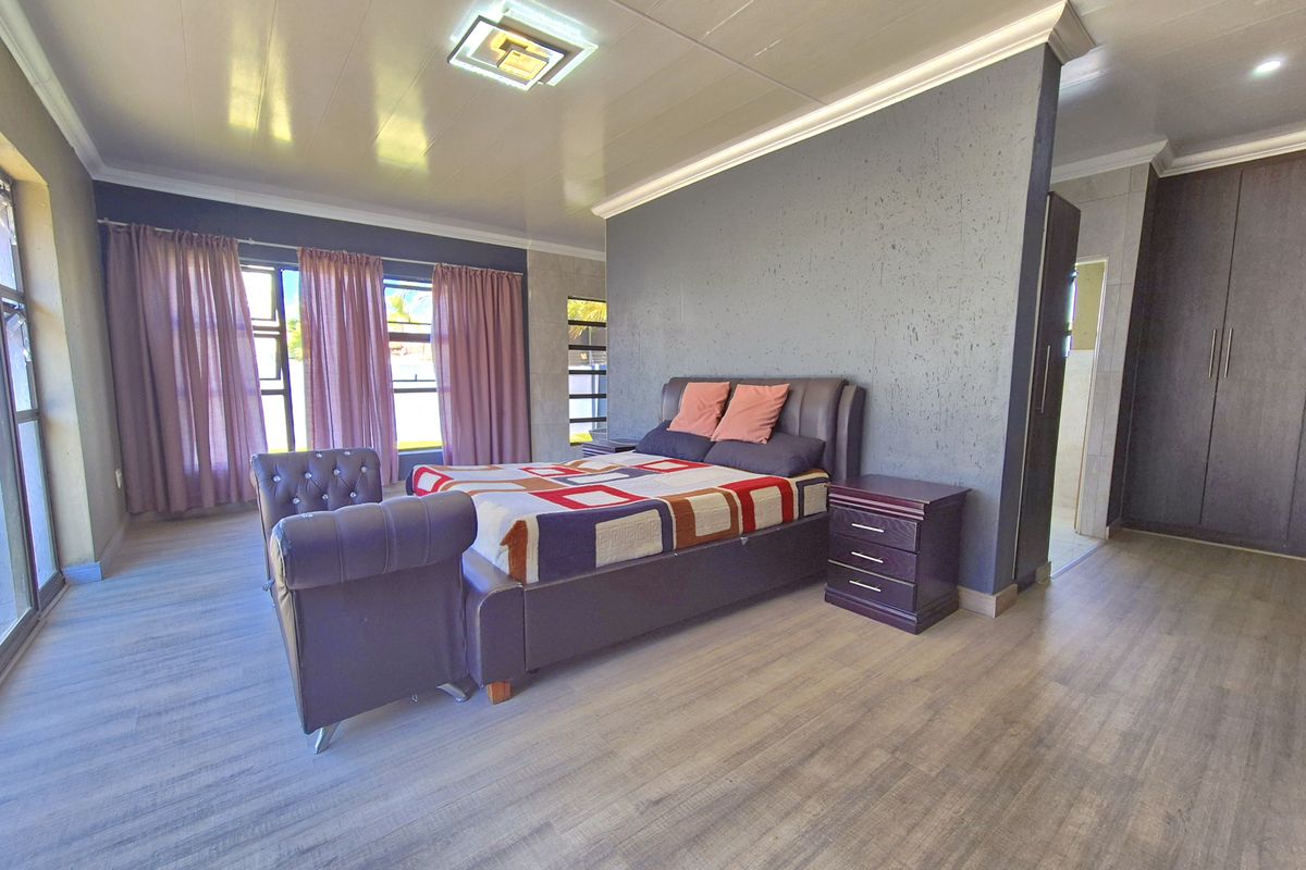 Spacious bedroom featuring modern wood-look flooring, a feature accent wall, built-in cupboards, and large windows allowing for ample natural light.