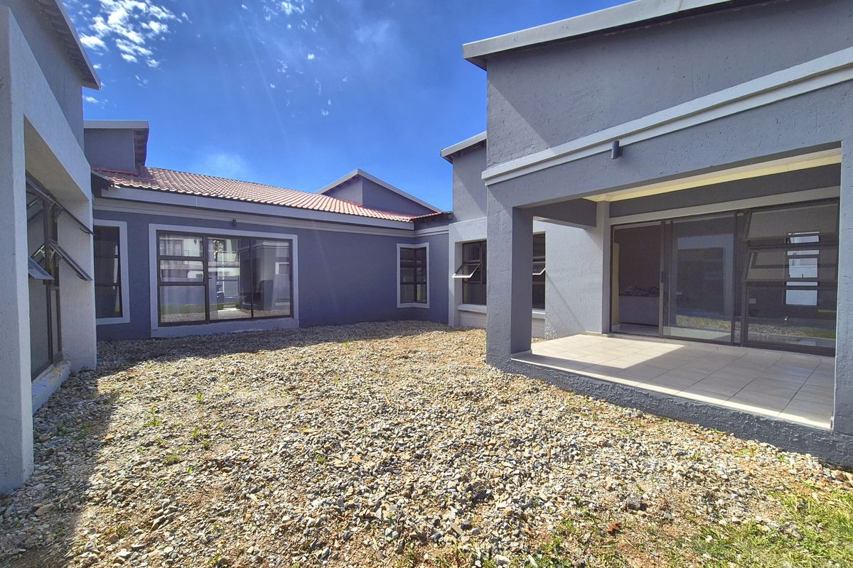 A rear view of the house featuring a covered patio area, large glass sliding doors, and a gravel-covered courtyard space.
