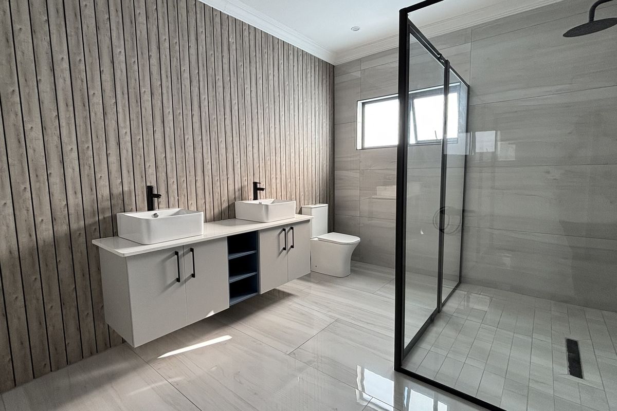 Modern bathroom featuring a double vanity with vessel sinks, a large walk-in shower with a glass screen, and contemporary wood-look wall paneling.