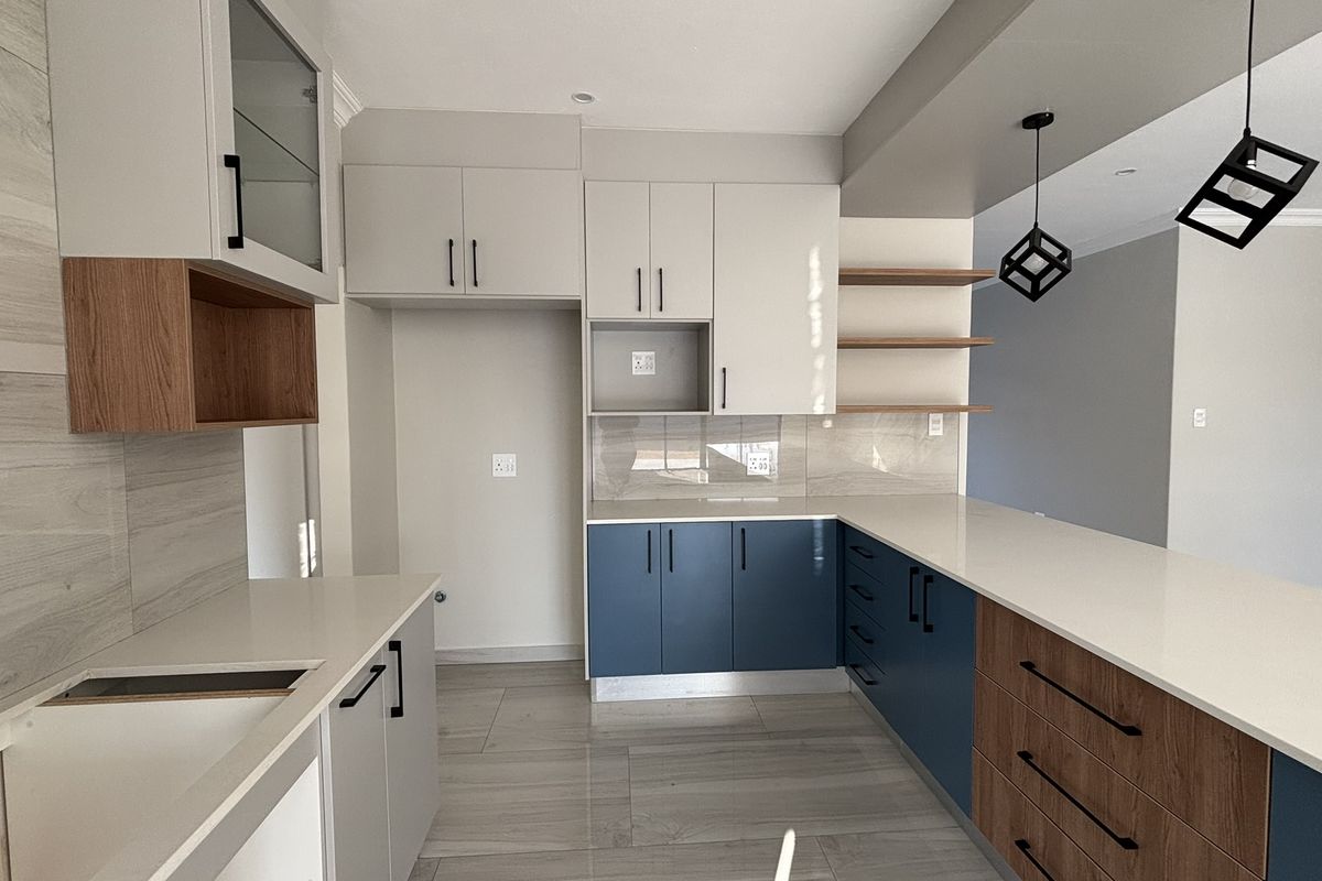 Modern kitchen featuring two-tone cabinetry, stone countertops, integrated shelving, and a breakfast bar with contemporary pendant lighting.