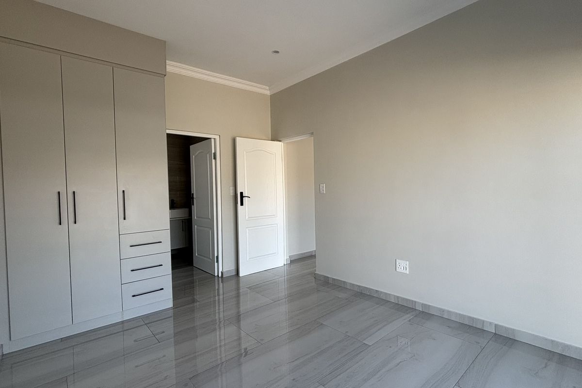 A bright, empty bedroom featuring modern grey tiled flooring, built-in cabinetry, and neutral wall finishes, providing a clean and versatile living space.