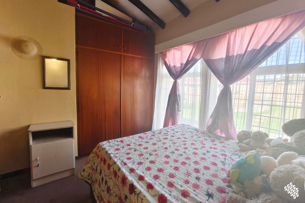 A bedroom featuring built-in wooden cupboards, exposed ceiling beams, and large windows allowing natural light.