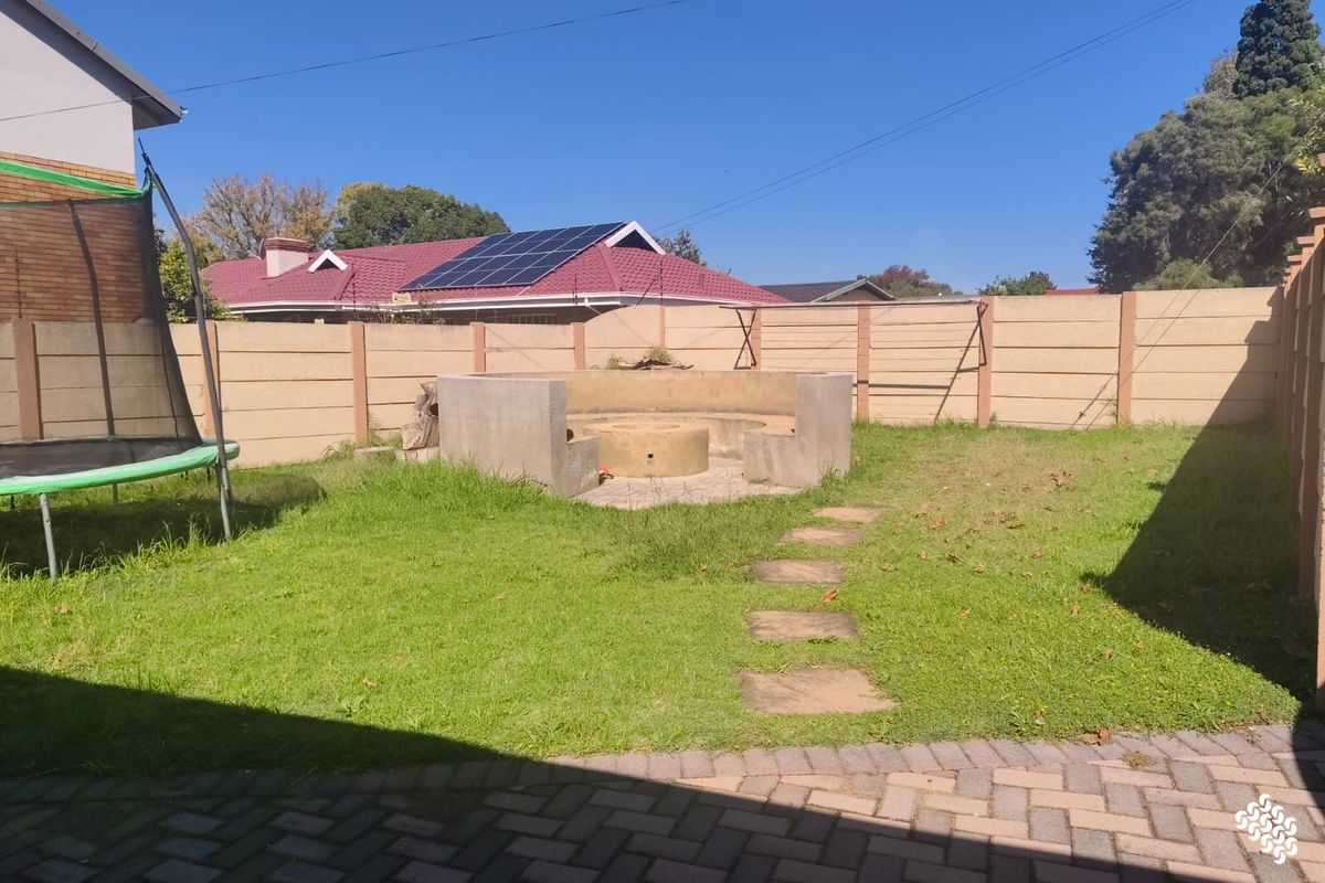A rear garden featuring a paved patio area, a built-in concrete fire pit, and perimeter boundary walling.