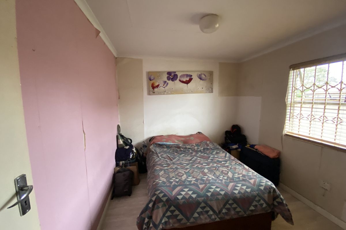 A bedroom featuring laminate flooring, a window with security bars, and walls requiring cosmetic attention and repainting.