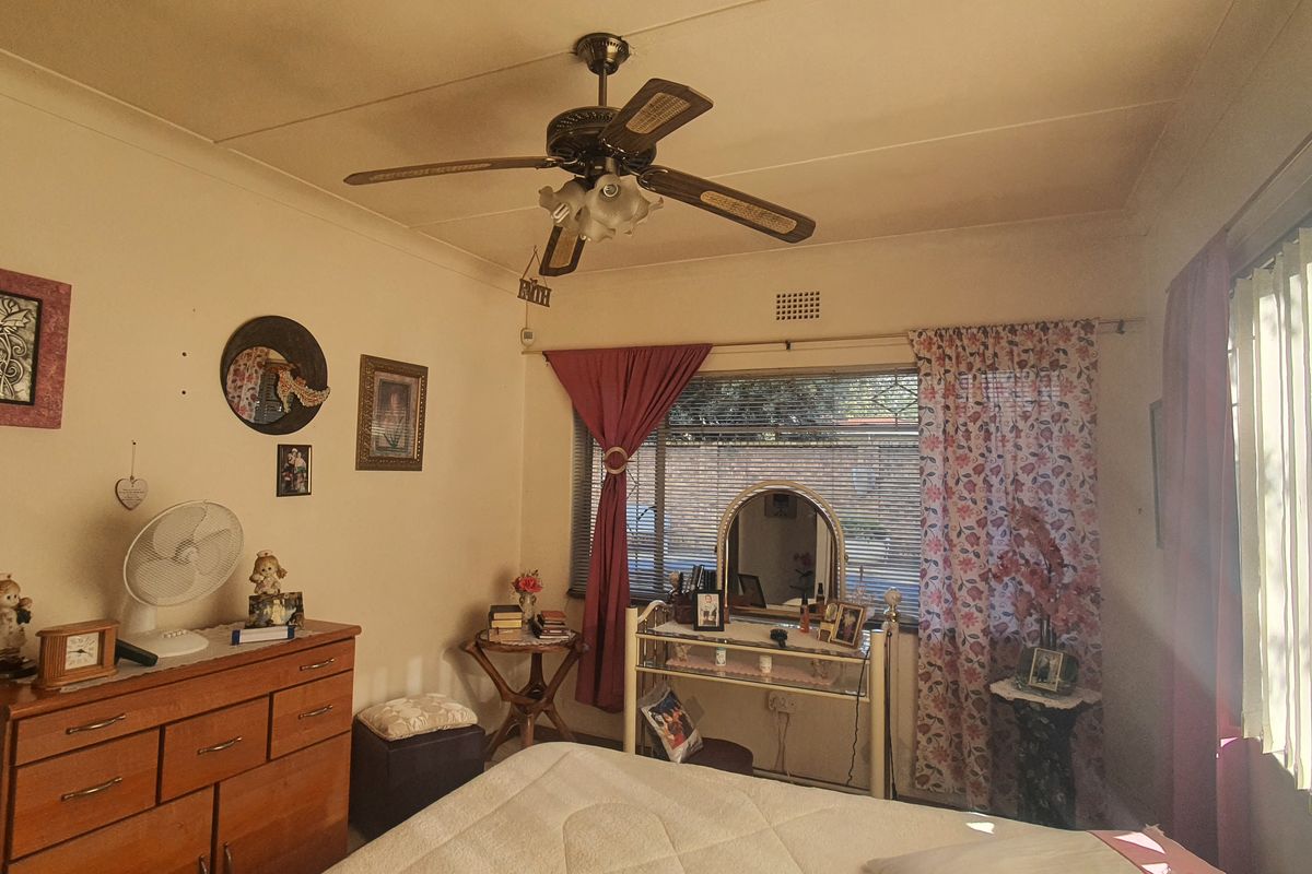 A bedroom featuring a ceiling fan, vertical blinds, and standard window treatments, offering a functional and lived-in space.