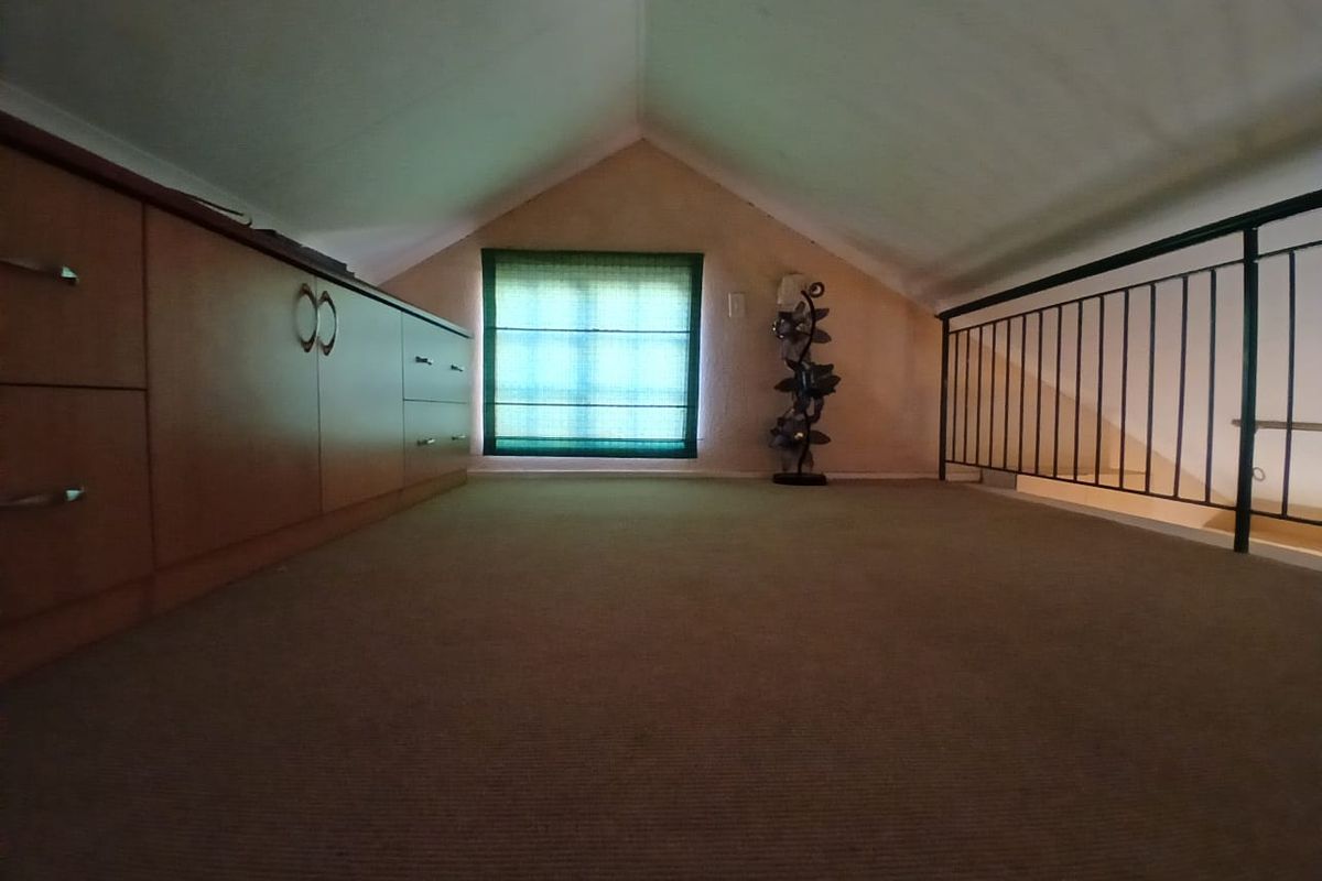 A loft-style bedroom or study area featuring built-in cabinetry, carpeted flooring, and a metal safety railing overlooking the lower level.