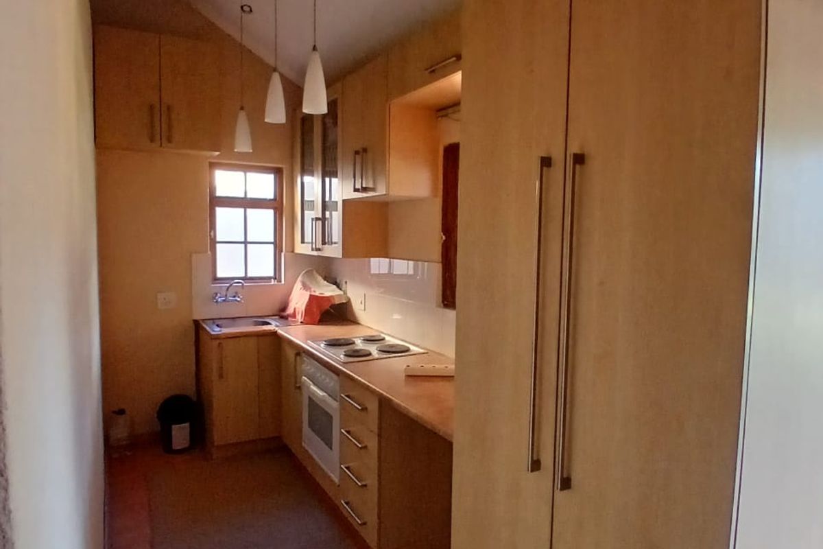 A compact galley-style kitchen featuring light wood cabinetry, a built-in oven, electric hob, and a stainless steel sink with tiled splashbacks.