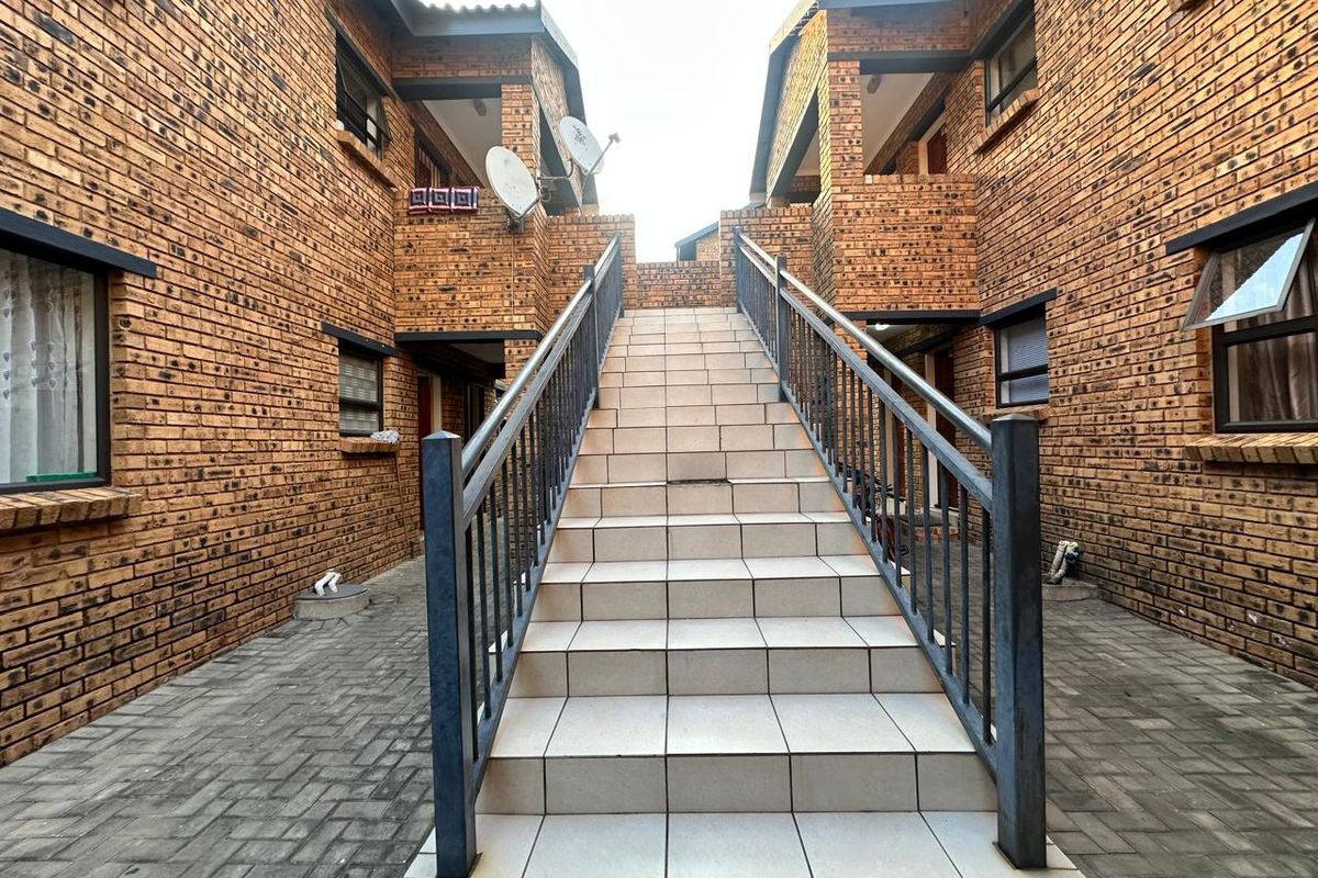 Exterior view of a face brick apartment complex featuring a central tiled staircase with metal balustrades and a paved courtyard area.