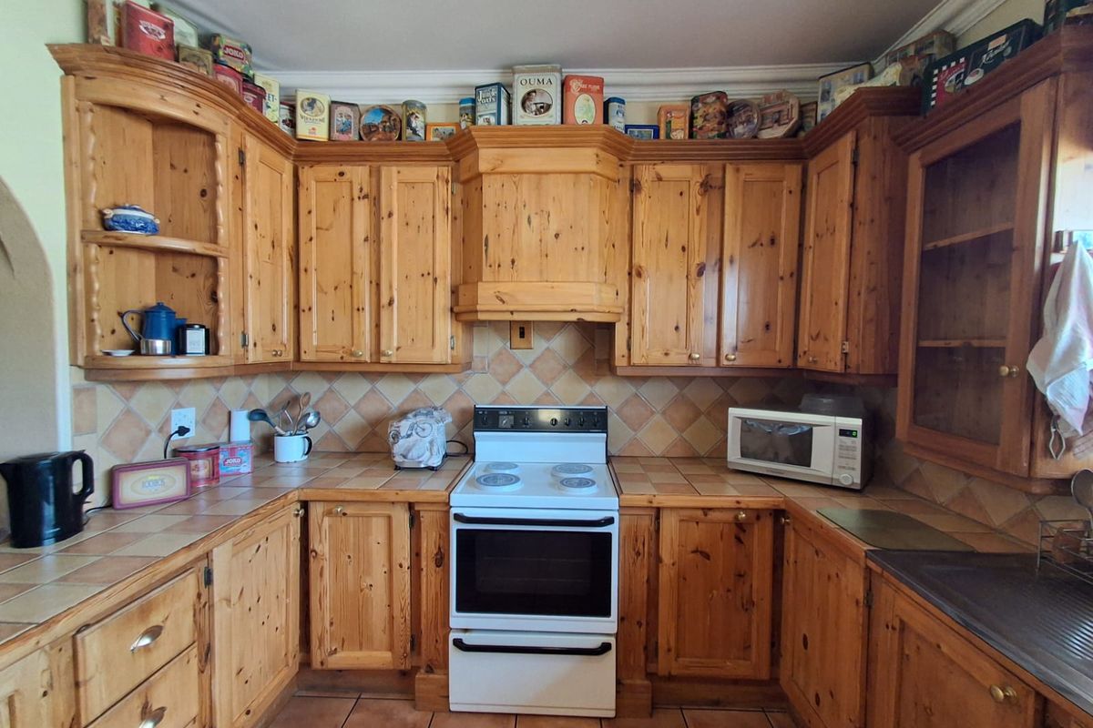 A traditional kitchen featuring solid wood cabinetry, tiled countertops, and a freestanding electric stove with an integrated extractor hood.