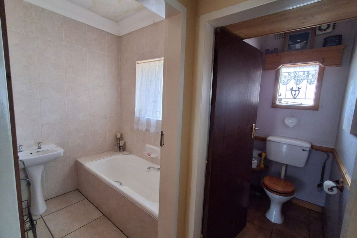 A split-layout bathroom featuring a tiled bathtub area with pedestal basin and a separate enclosed toilet room with traditional fixtures.