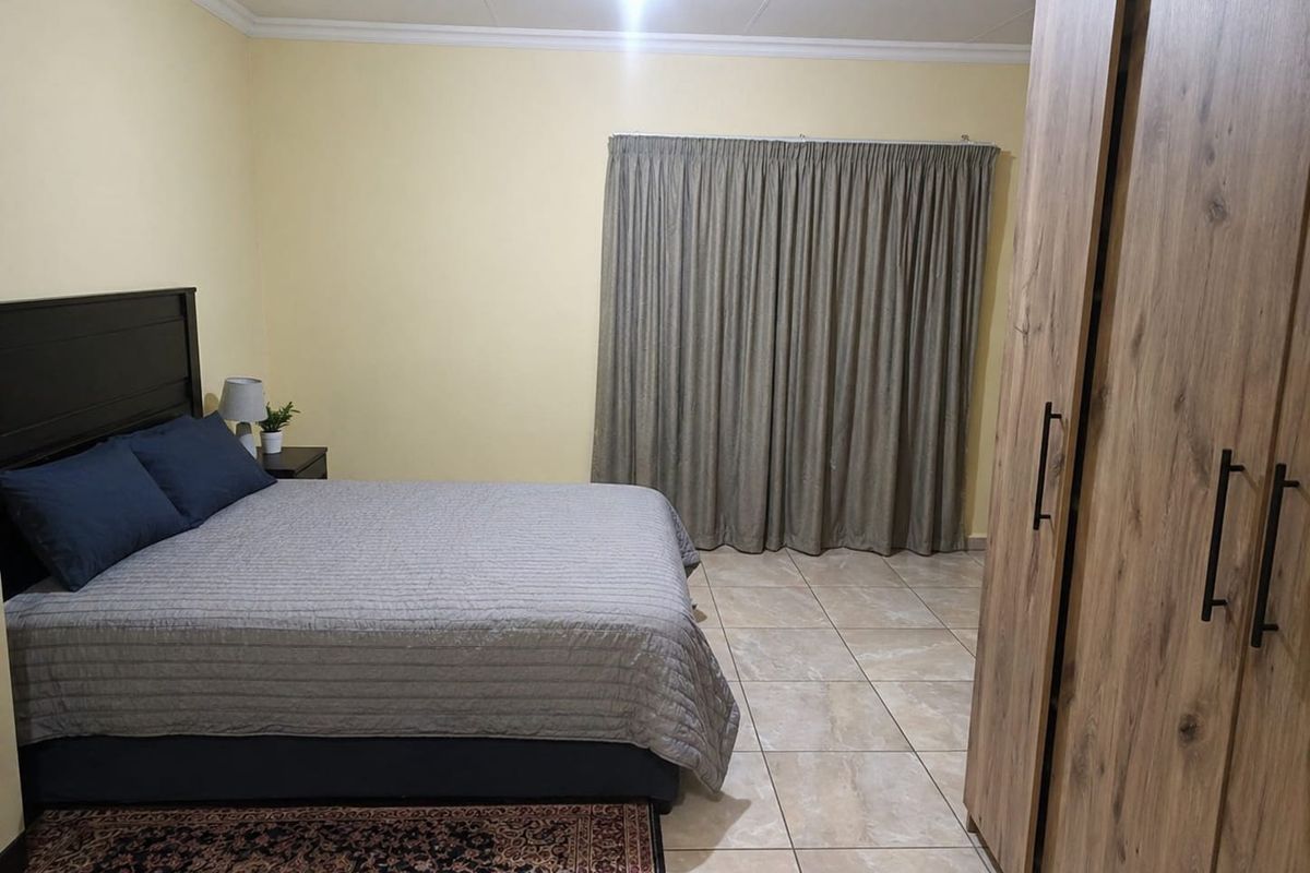 A spacious bedroom featuring neutral wall tones, tiled flooring, and built-in wooden cabinetry.
