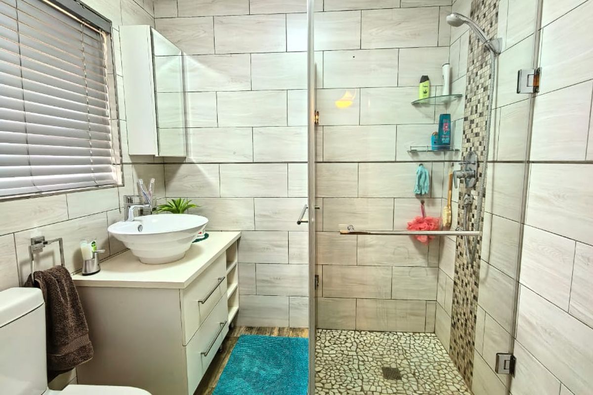 Modern bathroom featuring a glass-enclosed walk-in shower with pebble-style flooring, a vessel sink vanity, and wood-look tile flooring.