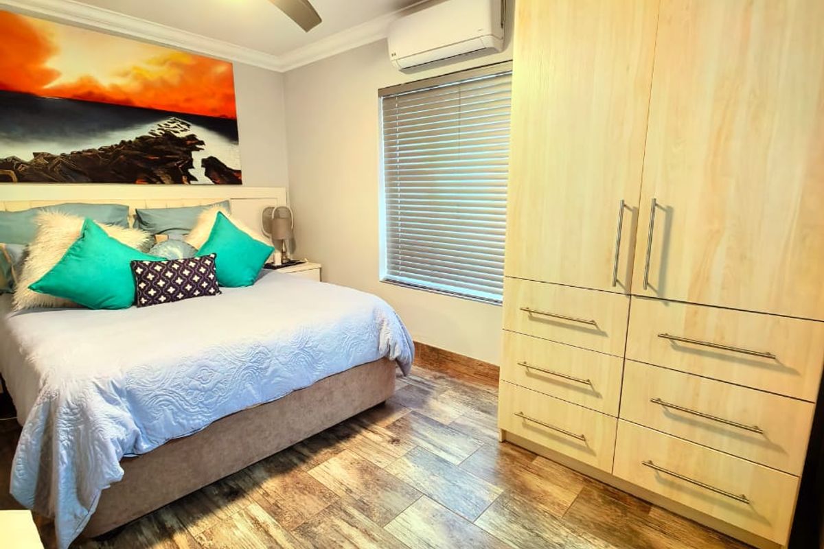 A well-maintained bedroom featuring wood-look tile flooring, a built-in wardrobe, a ceiling fan, and a wall-mounted air conditioning unit.