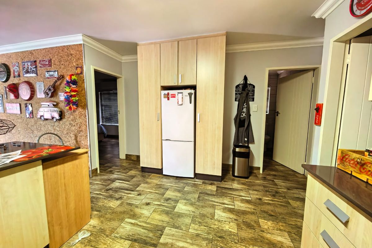A functional kitchen area featuring light wood-finish cabinetry, integrated storage, and durable wood-look tiled flooring, providing access to adjacent rooms.