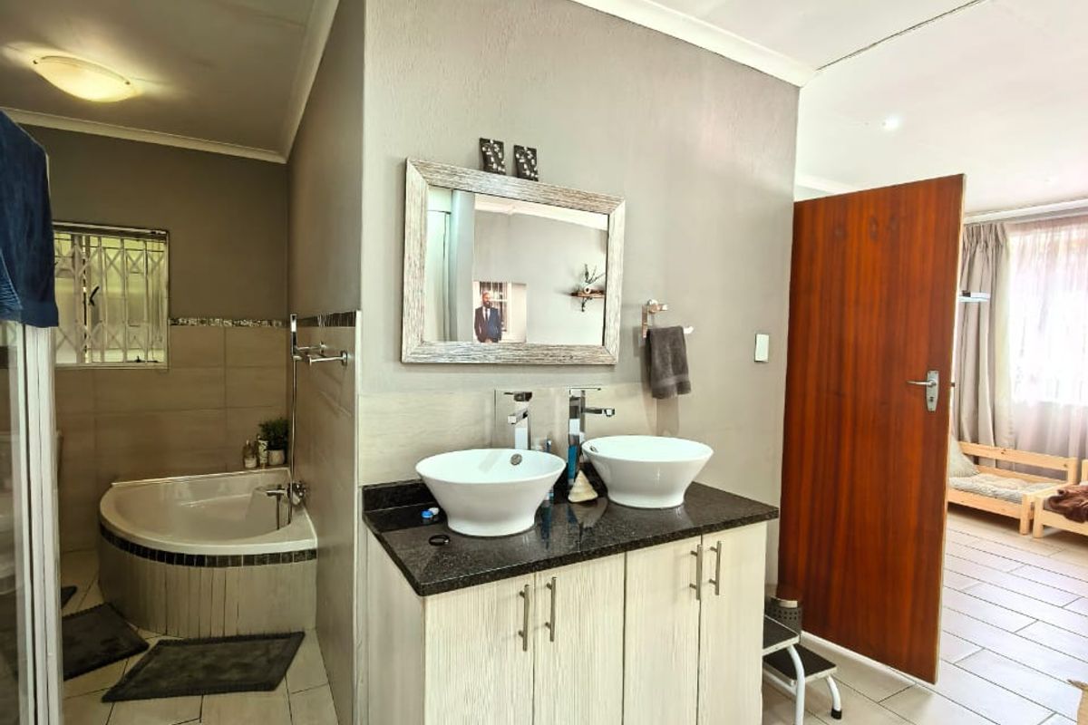 Bathroom featuring a double vanity with vessel sinks, granite countertop, corner bathtub, and tiled flooring, with an adjacent bedroom visible through the doorway.