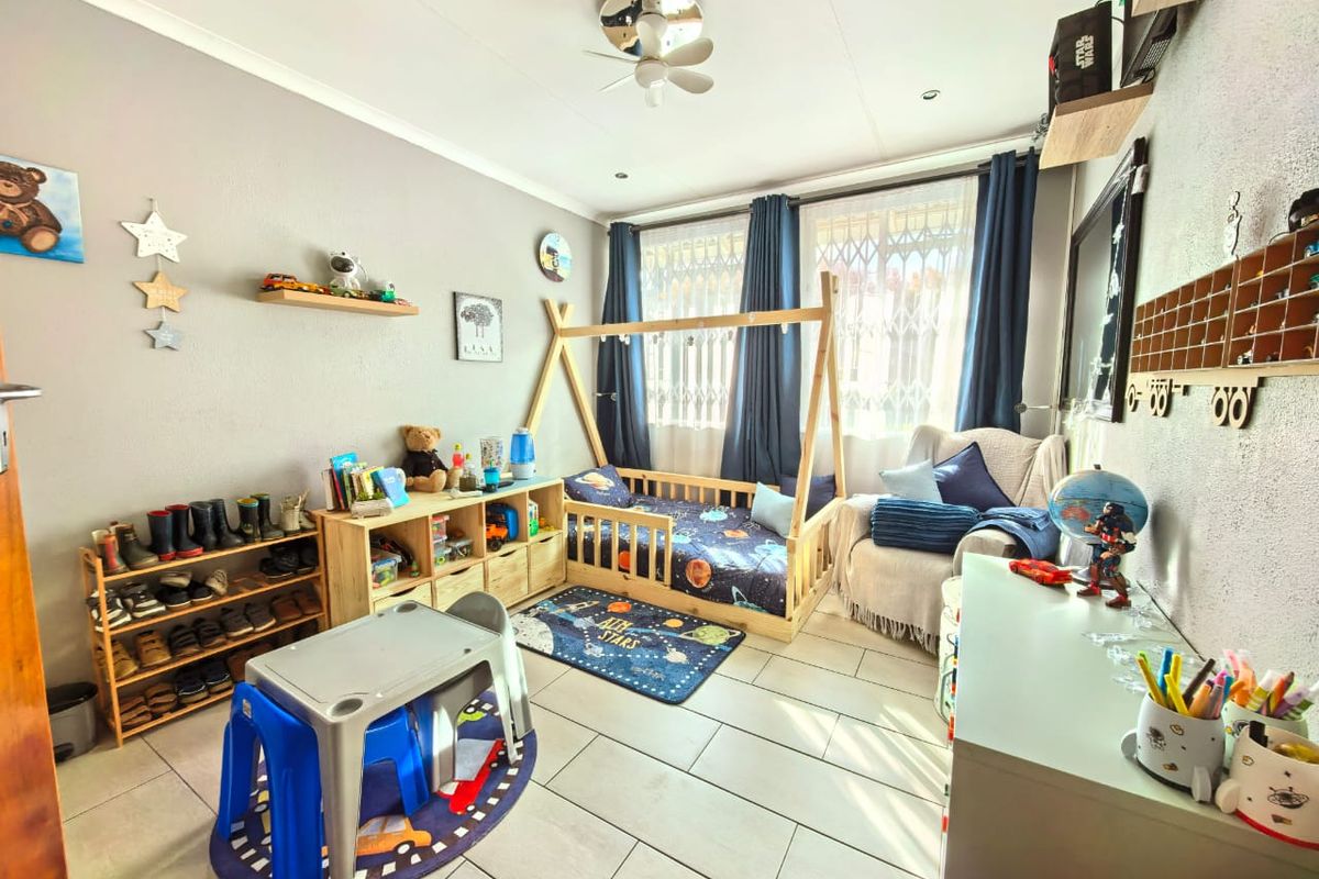 A well-maintained bedroom featuring tiled flooring, a ceiling fan, and large windows with security gates, providing ample natural light.