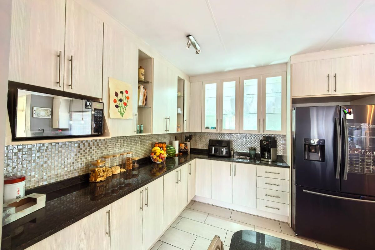 A well-maintained kitchen featuring light wood-grain cabinetry, dark granite countertops, a mosaic tile backsplash, and integrated storage solutions.