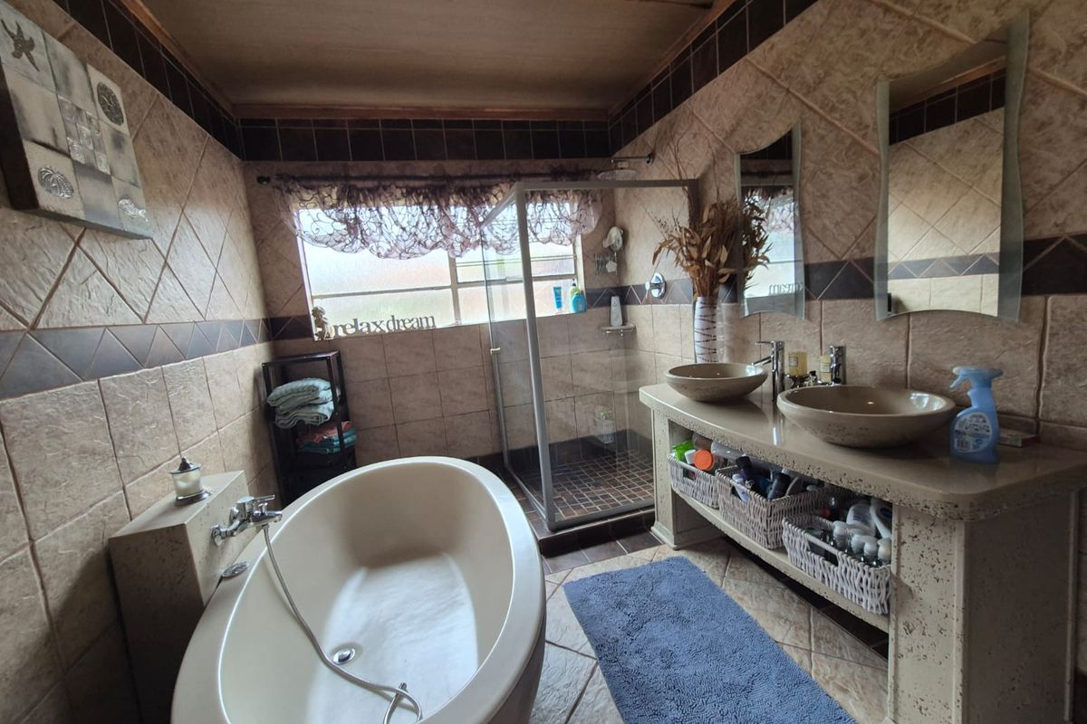 A bathroom featuring a freestanding bathtub, a glass-enclosed shower, and a dual-basin vanity with stone-look countertops and tiled walls.