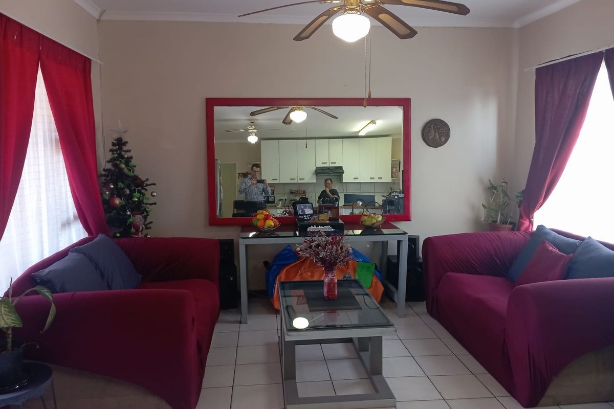 A living room featuring tiled flooring, a ceiling fan, and a large wall-mounted mirror reflecting the adjacent kitchen area.