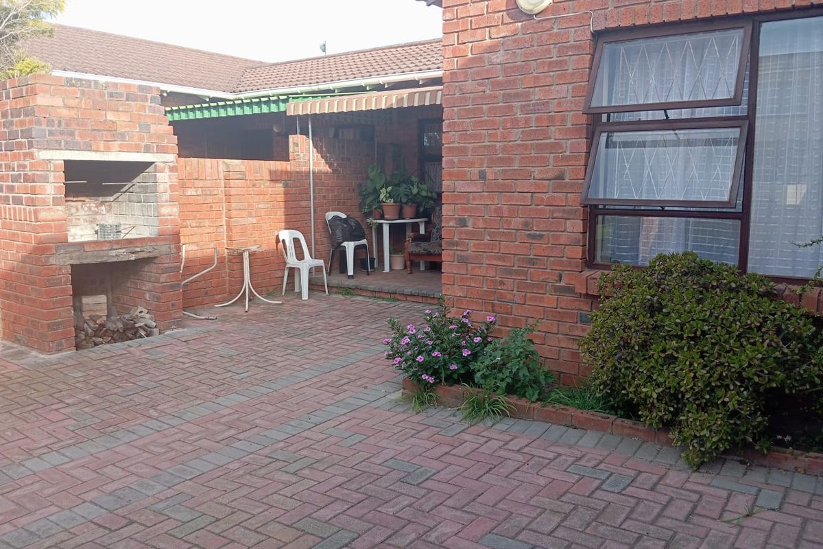 Rear courtyard area featuring a traditional brick built-in braai, paved flooring, and direct access to the main dwelling through top-hung windows.