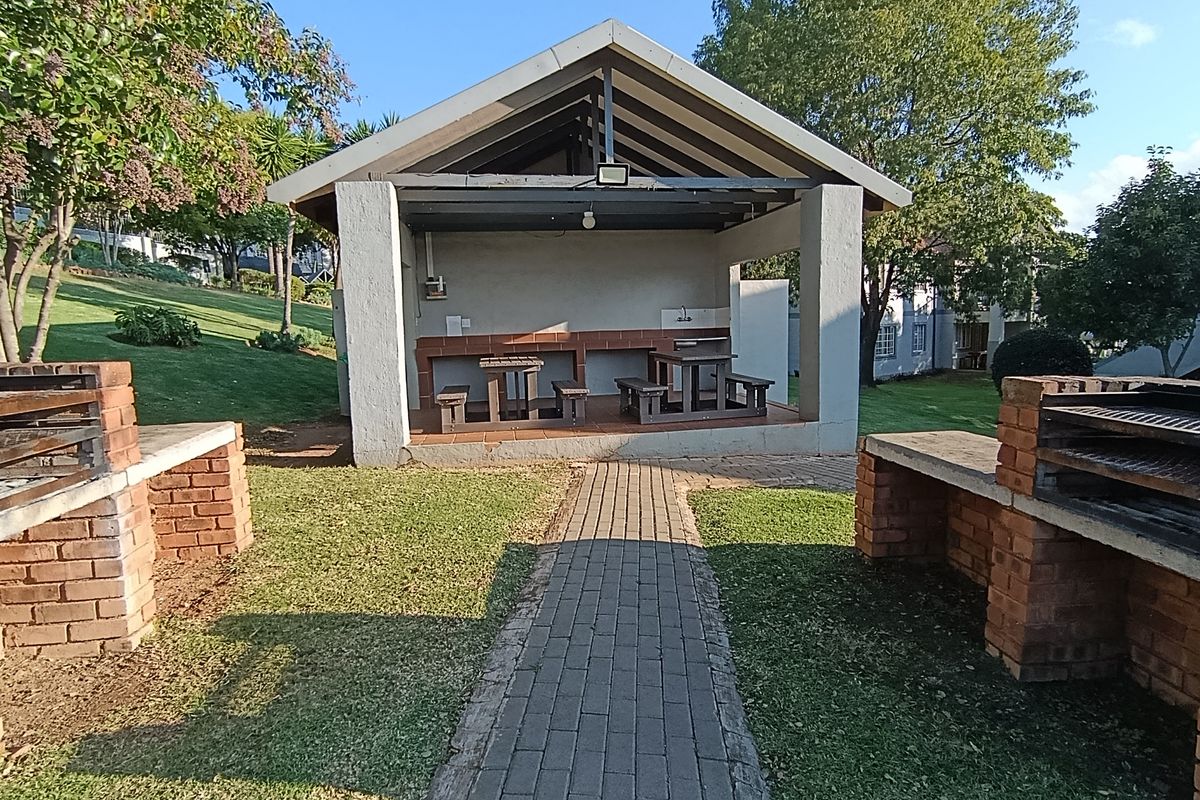 Outdoor communal entertainment area featuring a covered pavilion with built-in brick braai stations and paved walkways set within a landscaped garden.
