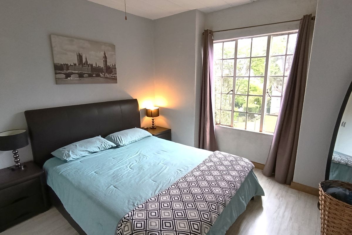 A well-lit bedroom featuring light-toned laminate flooring, a large multi-pane window, and neutral wall finishes.