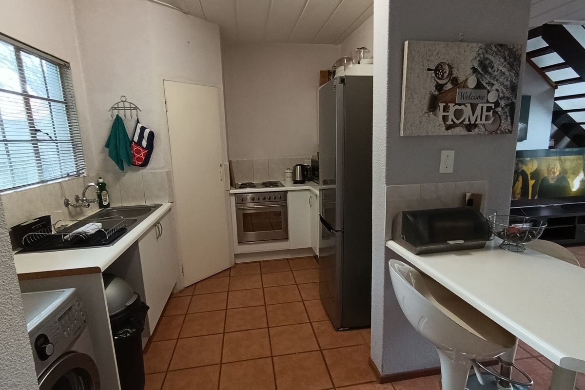 A functional kitchen featuring tiled flooring, built-in cabinetry, a stainless steel oven with hob, and a breakfast counter overlooking the living area.